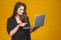 Young happy smiling woman in casual clothes holding laptop and sending email to her best friend isolated against yellow background Royalty Free Stock Photo