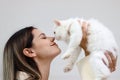 Young happy smiling woman holding cute white Persian cat and lift up her cat, try to kiss her pet, happy beautiful lady playing Royalty Free Stock Photo