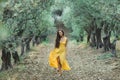 Young happy smiling woman walking olive tree garden. Yellow linen summer dress Royalty Free Stock Photo