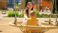 Young happy smiling woman oushing her toddler son swinging on the playground Royalty Free Stock Photo