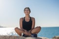 Young happy sportswoman sitting on rock at seaside