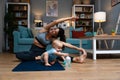 Young happy successful independent single mother is practicing yoga at home on a yoga mat while her baby is carelessly sitting on Royalty Free Stock Photo