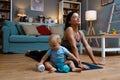 Young happy successful independent single mother is practicing yoga at home on a yoga mat while her baby is carelessly sitting on Royalty Free Stock Photo