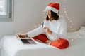 Young happy teen girl in red santa hat shopping online buying Christmas gifts paying by credit card using laptop Royalty Free Stock Photo