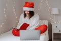 Young happy teen girl in red santa hat shopping online buying Christmas gifts using laptop Royalty Free Stock Photo