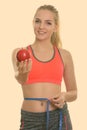 Young happy teenage girl smiling while giving red apple and measuring waist ready for gym Royalty Free Stock Photo