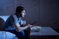 Young happy television addict man sitting on home sofa watching TV eating popcorn