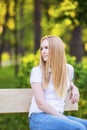 Young, happy, thin young blond woman with long beautiful hair, smiling, in the summer park under the rays of the sun