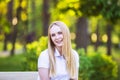 Young, happy, thin young blond woman with long beautiful hair, smiling, in the summer park under the rays of the sun