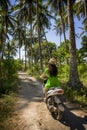 Young happy tourist woman with hat riding scooter motorbike in tropical paradise jungle with blue sky and palm trees exploring tr Royalty Free Stock Photo