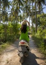 Young happy tourist woman with hat riding scooter motorbike in tropical paradise jungle with blue sky and palm trees exploring tr Royalty Free Stock Photo