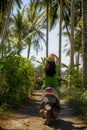 Young happy tourist woman with hat riding scooter motorbike in tropical paradise jungle with blue sky and palm trees exploring tr Royalty Free Stock Photo