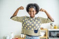 Young happy woman african american afro hair standing and making strong hand while drinking a milk for breakfast with fun