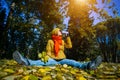 Young happy woman in autumn park on sunny day, drinking coffee or tea, sitting on falling foliage, having fun with yellow leaves. Royalty Free Stock Photo