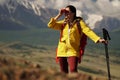 Young happy woman with backpack standing on a rock and looking through binocular to a valley below. Royalty Free Stock Photo