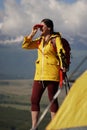 Young happy woman with backpack standing on a rock and looking through binocular to a valley below. On the cliff is a Royalty Free Stock Photo