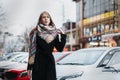 Young happy woman blonde in a black coat and scarf walks through city. Waiting for meeting Royalty Free Stock Photo