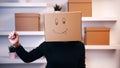 Young happy woman with a cardboard box over head with drawn emoji dancing in the new apartment