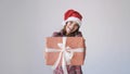 Young happy woman in Christmas cap gives a gift box on a white background. Small present in woman hands. Holidays Royalty Free Stock Photo