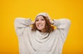 Young happy woman with curly hair in winter hat standing over yellow background smiling with happy face holding her head Royalty Free Stock Photo