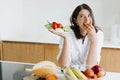 Young happy woman eating cherry tomato and holding plate with green lettuce, arugula and tomato on background of modern white Royalty Free Stock Photo