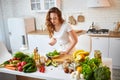 Young happy woman eating salad in the beautiful kitchen with green fresh ingredients indoors. Healthy food concept Royalty Free Stock Photo