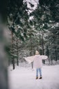 Woman stands with raised arms in white sheepskin coat, hat and scarf in snowy winter forest Royalty Free Stock Photo