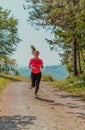 Young happy woman enjoying in a healthy lifestyle while jogging on a country road through the beautiful sunny forest Royalty Free Stock Photo