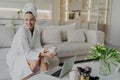 Young happy woman freelancer in bathrobe drinking tea and working remotely on laptop Royalty Free Stock Photo