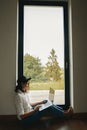 Young happy woman in hat using laptop, shopping or working online from home. Stylish hipster girl with laptop sitting on floor at Royalty Free Stock Photo