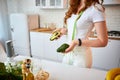 Young happy woman holding avocado for making salad in the beautiful kitchen with green fresh ingredients indoors. Healthy food and Royalty Free Stock Photo