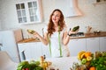 Young happy woman holding avocado for making salad in the beautiful kitchen with green fresh ingredients indoors. Healthy food and Royalty Free Stock Photo