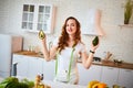 Young happy woman holding avocado for making salad in the beautiful kitchen with green fresh ingredients indoors. Healthy food and Royalty Free Stock Photo