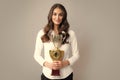 Young happy woman holding a champion cup on gray background. Portrait of young woman with gold trophy cup. Successful Royalty Free Stock Photo