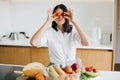 Young happy woman holding cherry tomato at eyes and showing kiss on background of modern white kitchen. Healthy food concept. Home Royalty Free Stock Photo