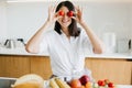 Young happy woman holding cherry tomato at eyes and smiling on background of modern white kitchen. Healthy food concept. Home Royalty Free Stock Photo