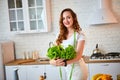 Young happy woman holding lettuce leaves for making salad in the beautiful kitchen with green fresh ingredients indoors. Healthy Royalty Free Stock Photo