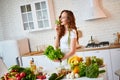 Young happy woman holding lettuce leaves for making salad in the beautiful kitchen with green fresh ingredients indoors. Healthy Royalty Free Stock Photo