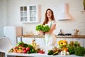 Young happy woman holding lettuce leaves for making salad in the beautiful kitchen with green fresh ingredients indoors. Healthy Royalty Free Stock Photo