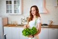 Young happy woman holding lettuce leaves for making salad in the beautiful kitchen with green fresh ingredients indoors. Healthy Royalty Free Stock Photo