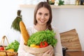 Young happy woman is holding paper bag full of vegetables and fruits while smiling in kitchen. Housewife have made Royalty Free Stock Photo