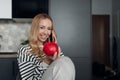 Young happy woman holding red apple and smiling talking about new diet by smart phone. Portrait of lady in home clothes Royalty Free Stock Photo