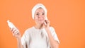 Young happy woman holds empty white bottle. Caucasianl woman cleaning her face on orange background. Skin care concept