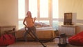 Young happy woman is hoovering the floor at home using modern vacuum cleaner and listening to music with headphones Royalty Free Stock Photo