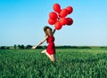 Young happy woman jumping with red balloons on green summer field Royalty Free Stock Photo