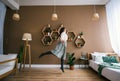 Young happy woman jumping up in living room with large sunny window in apartment Royalty Free Stock Photo