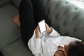 Young happy woman lie down on couch and playing smart phone with blank screen.