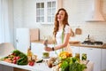 Young happy woman preparing tasty salad in the beautiful kitchen with green fresh ingredients indoors. Healthy food and Dieting