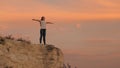 Young happy woman raises her hands up, standing on top of a mountain above sea against backdrop of blue sky. Watching Royalty Free Stock Photo