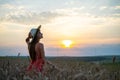 Young happy woman in red summer dress and white straw hat walking on yellow farm field with ripe golden wheat enjoying warm Royalty Free Stock Photo